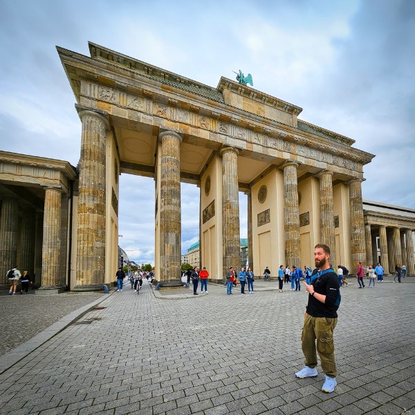 Eran standing in front of the Brandenburg Gate in Berlin, people in the background on a cloudy day.