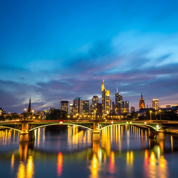 Frankfurt skyline at dusk with lights of building and bridge reflecting off the river Main.